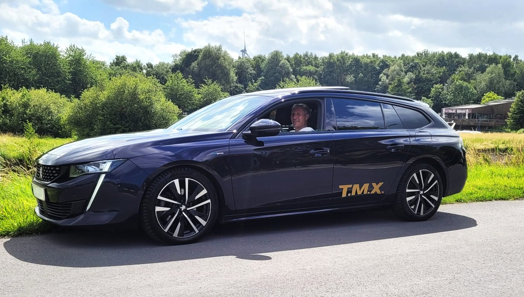 Donkerblauwe Peugeot 508 break van Taxi T.M.X. met gouden belettering langs de weg